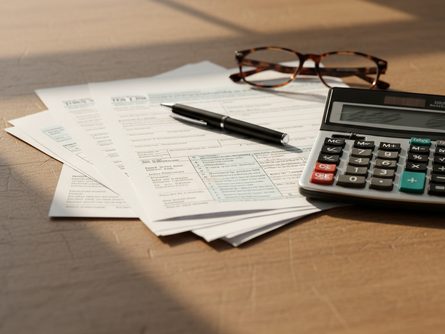 책상 위에 놓인 세금 신고 서류, 계산기, 볼펜, 안경