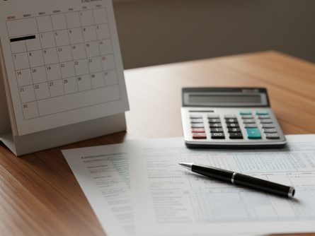나무 책상 위에 놓인 달력, 계산기, 세금 서류와 볼펜