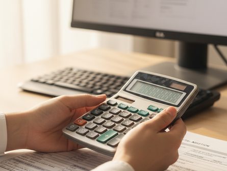 밝은 사무실 공간에서 손으로 잡은 계산기와 연말정산 서류 클로즈업, 뒤로 흐릿하게 보이는 모니터와 키보드